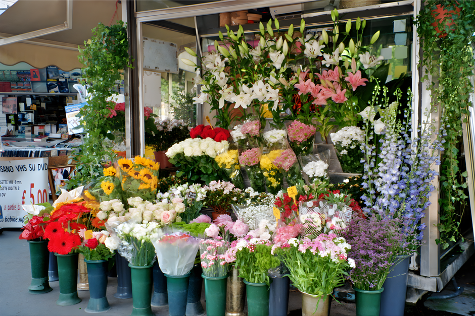 A vibrant floral display outside a street-side flower shop featuring a variety of fresh flowers arranged in bouquets and potted plants. Prominent are white lilies with large, trumpet-shaped petals and
