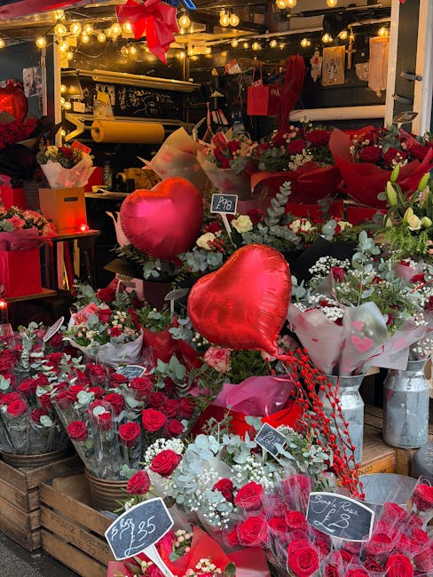 A floral display featuring a variety of fresh flowers arranged in bouquets and baskets, predominantly in shades of red, pink, and white. The display includes red roses, white lilies, and smaller decor