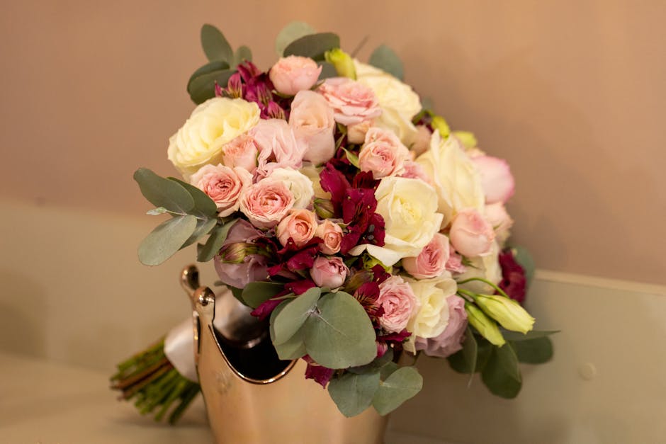A bouquet arrangement of fresh flowers featuring pale pink roses, white roses, and deep burgundy blooms, complemented by silvery-green eucalyptus leaves. The flowers are densely packed and arranged in